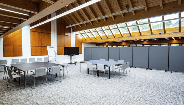 large meeting space with two large tables with chairs round them. the room has windows up high with wooden panelling across the roof